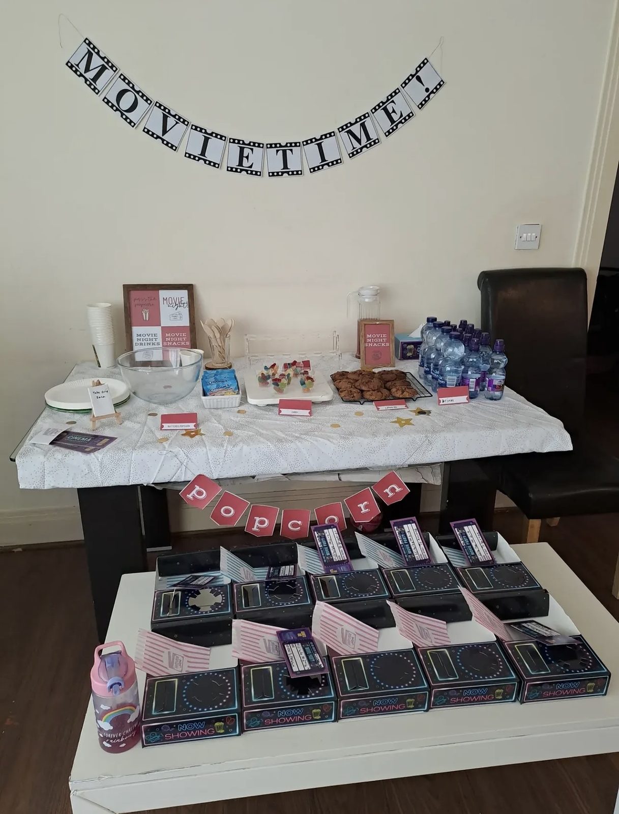 Movie night party table with bunting, a row of black neon snack trays on a white table
