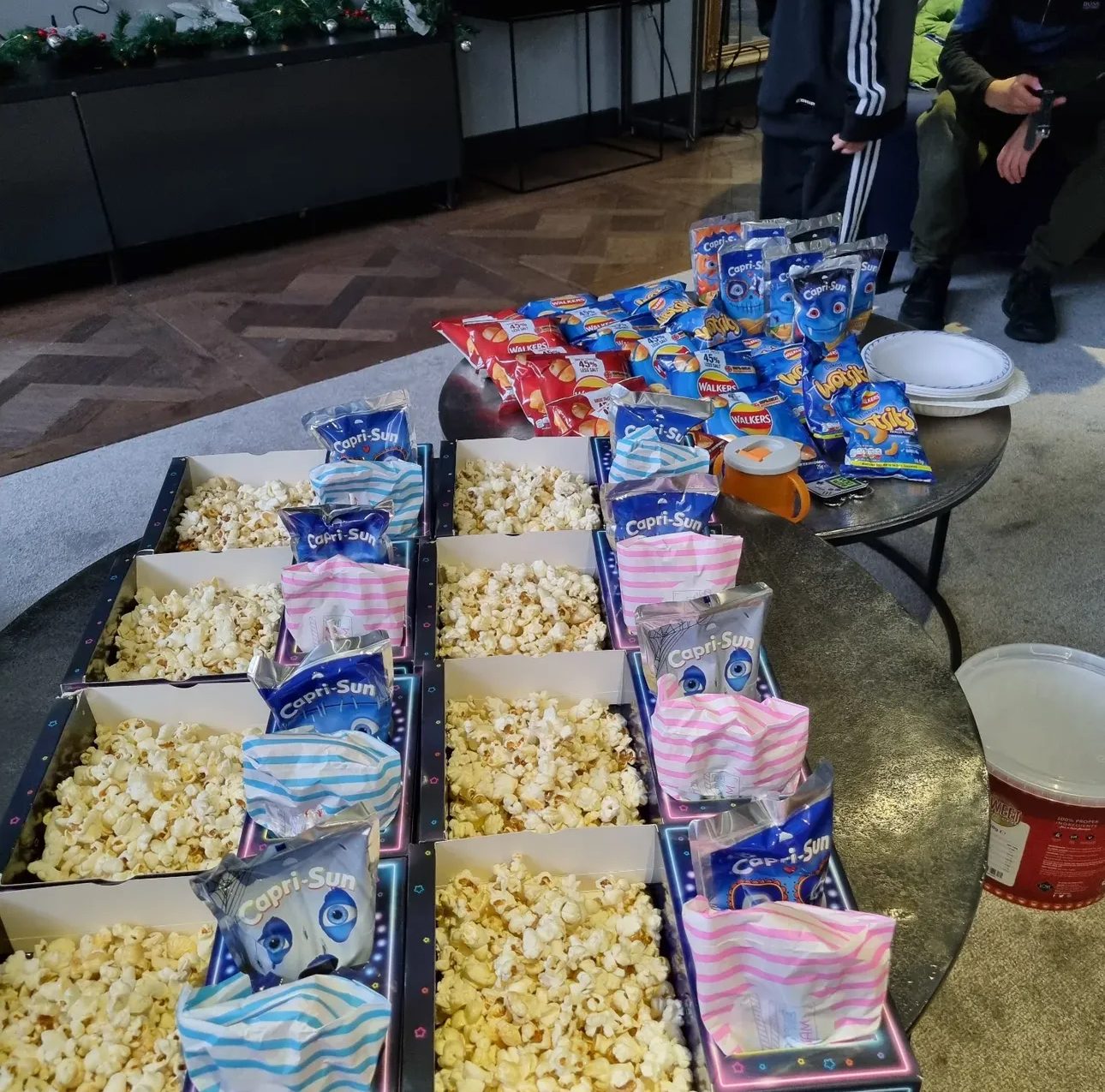 Many popcorn-filled snack trays with striped bags and crisps lined up on a party table