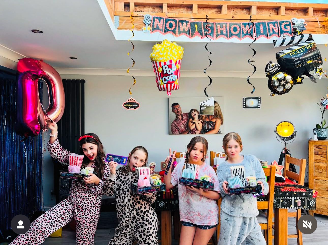 Group of girls in pyjamas holding snack trays in a room decorated with Now Showing bunting and balloons