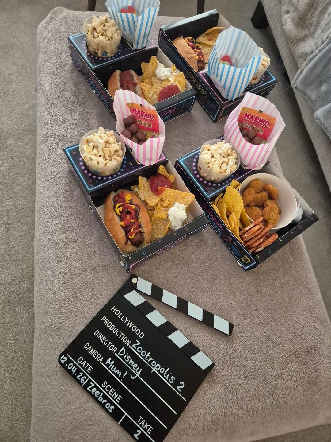 Overhead view of several filled snack trays on a grey ottoman beside a film clapperboard