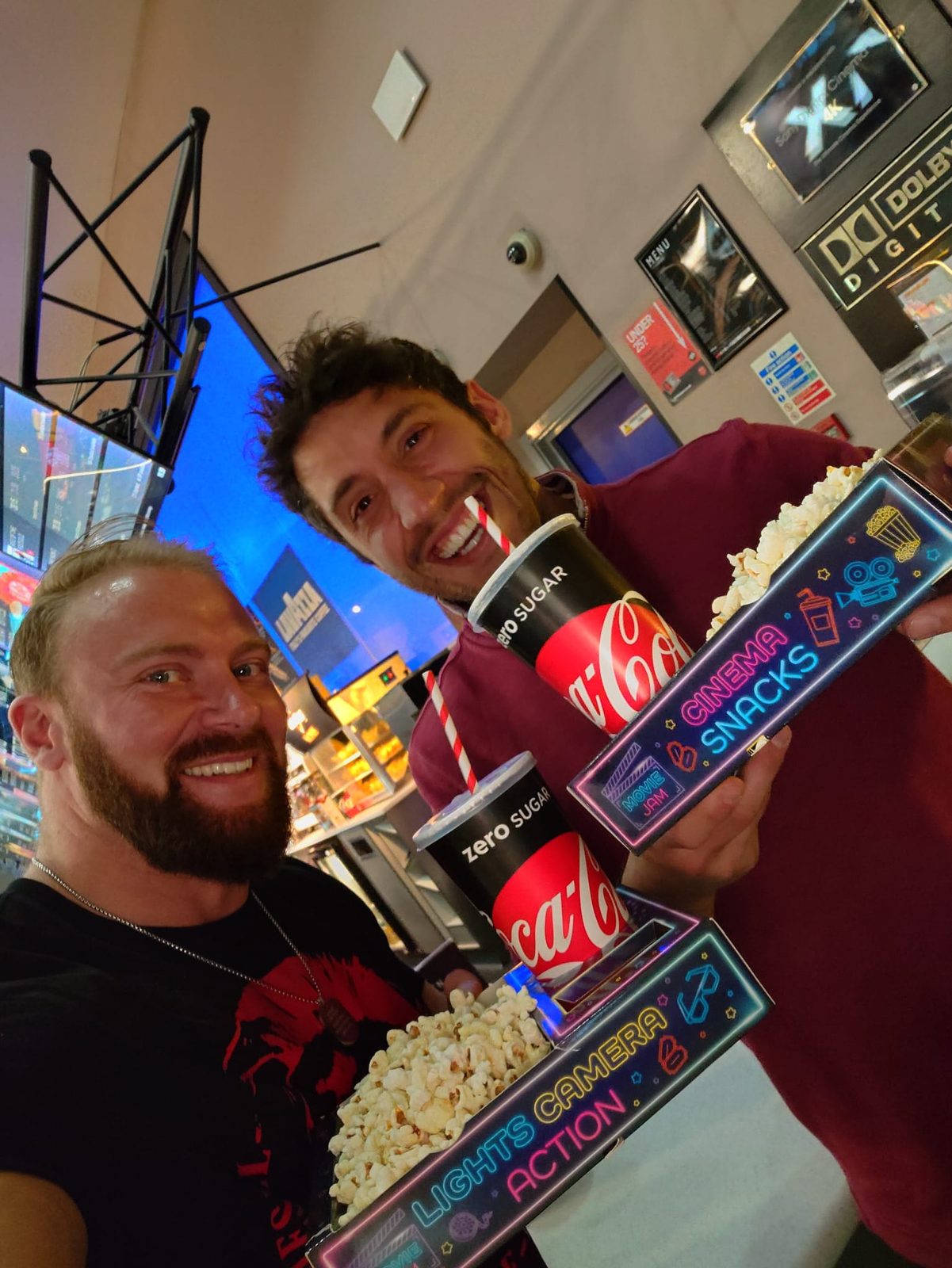 Two men at a cinema holding neon snack trays with popcorn and cola cups