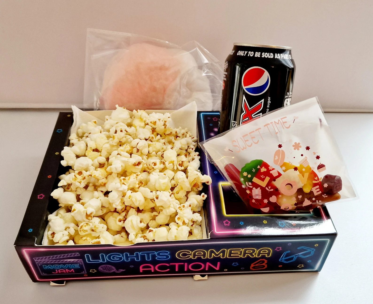 Neon snack tray filled with popcorn, a cola can and a small sweets pouch