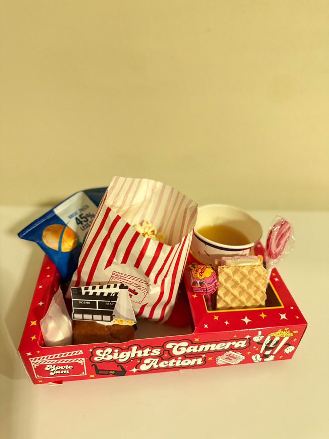 Red Lights Camera Action snack tray with striped popcorn bag, drink and treats against a yellow wall